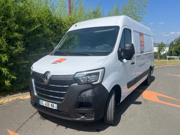 Camionnette Renault blanche stationnée devant des arbres.